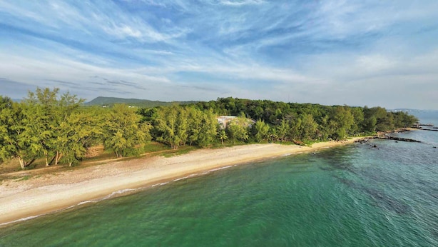 A coastal landscape with a sandy beach, clear turquoise waters, and dense green foliage. - The Aurora Retreat (Phu Quoc)
