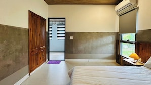 A bedroom with a bed, a window with a lamp, a door, and an air conditioning unit. - The Aurora Retreat (Phu Quoc)