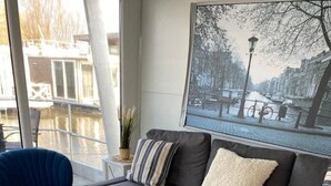 A modern living room with a grey sofa, a blue armchair, and a wicker basket on a white table. - Unique Houseboat near Amsterdam (20 min) (Monnickendam)