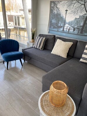 Een moderne woonkamer met een grijze bank, een blauwe fauteuil en een rieten mand op een witte tafel.