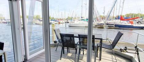 A boat deck with a table and chairs, a view of the marina with boats, and a glass door leading to the water.
