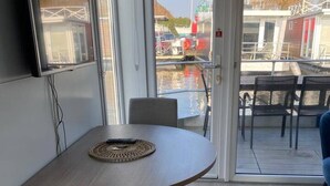 A modern interior with a round table and chairs, a television mounted on the wall, and a view of the outside through a glass door. - Unique Houseboat near Amsterdam (20 min) (Monnickendam)