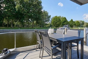 An outdoor deck with a table and chairs, overlooking a body of water and a park with trees.