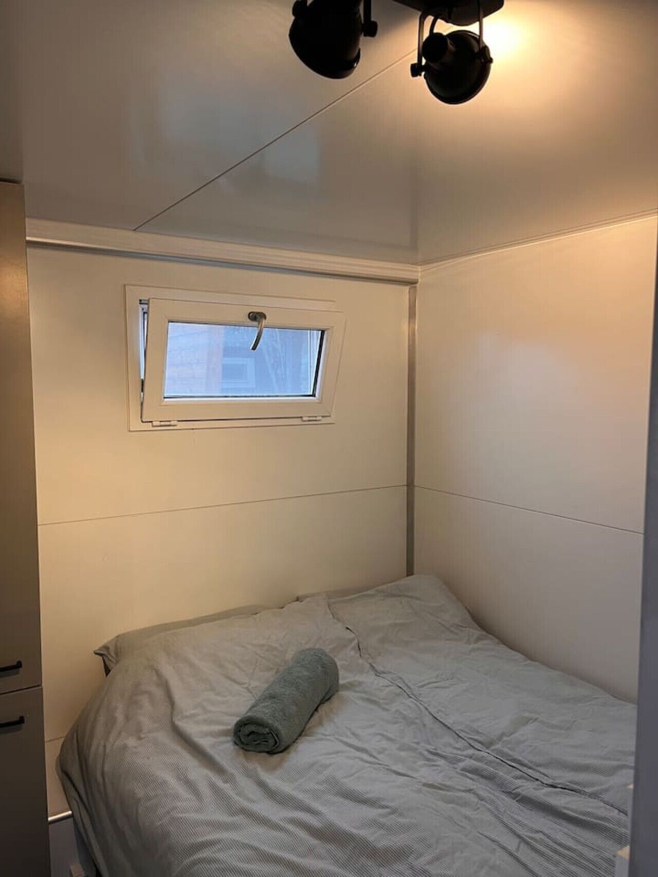 Una habitación pequeña con cama individual, ventana y lámpara en el techo.