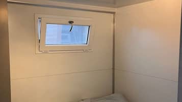 Una habitación pequeña con cama individual, ventana y lámpara en el techo.