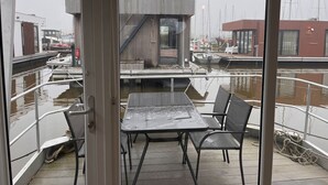 A view from a ship's deck with a table and chairs, a railing, and a view of the water and docked boats. - Fantastic Houseboat, 15 min Amsterdam Free Parking (Monnickendam)