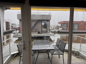 Uitzicht vanaf het scheepsdek, met een tafel, stoelen, een reling en zicht op het water en liggende boten.