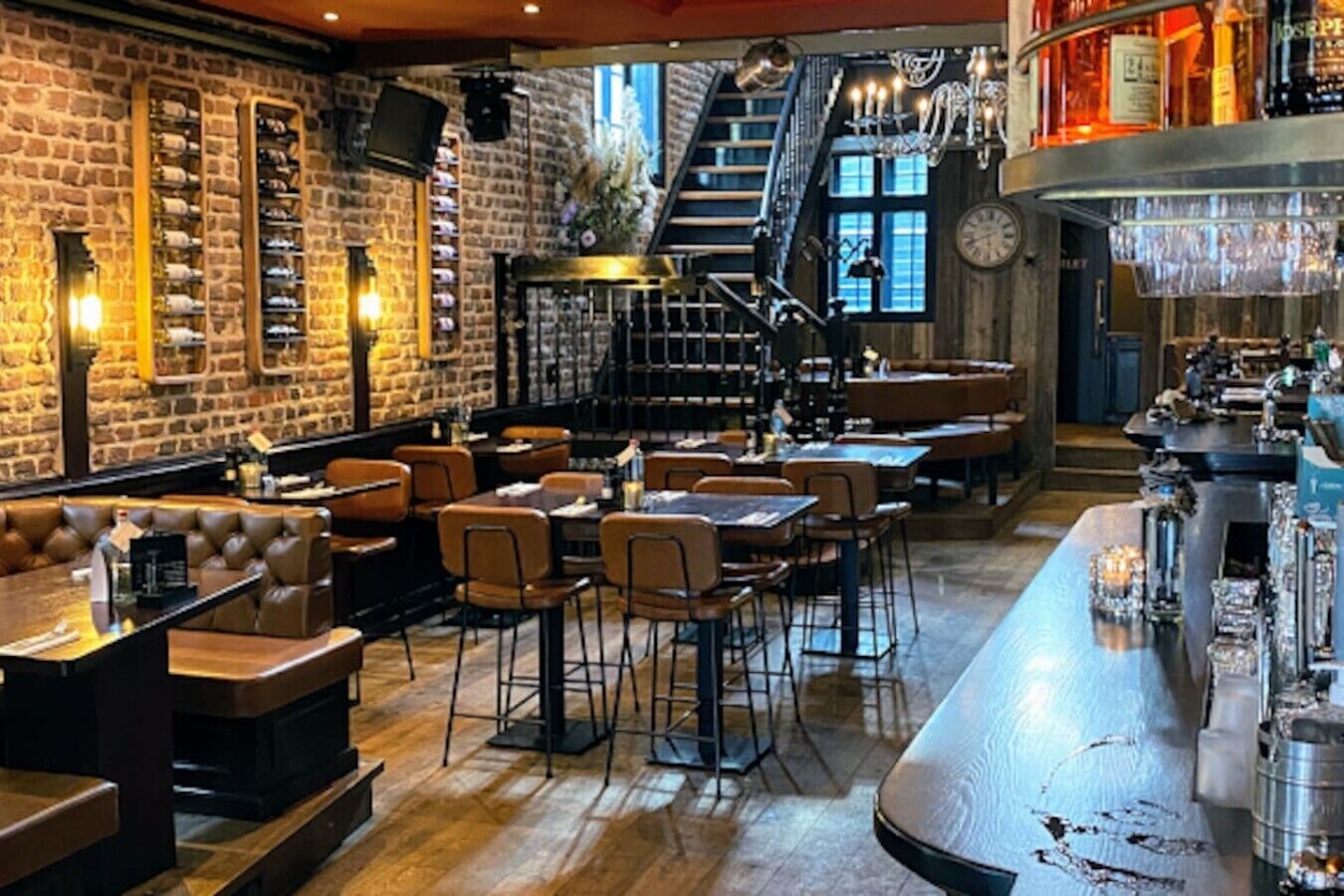 A restaurant with brick walls, wooden flooring, and a bar area with bottles and glasses.