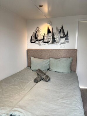 Een bed met hoofdeinde, twee kussens en een opgerolde deken.