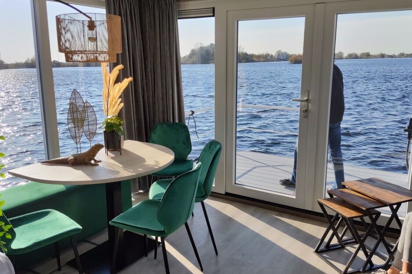 Habitación con mesa, sillas y vistas al agua, con una persona de pie cerca de la puerta.