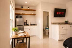 Eine moderne Küche mit einem eingebauten Kühlschrank, einem Esstisch mit Tellern und Gläsern sowie einem an der Wand befestigten Fernseher, der 'NETFLIX' anzeigt.