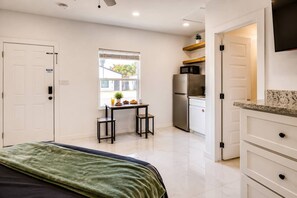 A compact hotel room with a bed, a small kitchenette, a dining table with breakfast, and a view of the outside. - #15 | South Padre Getaway | Studio + Pool | Relax (South Padre Island)