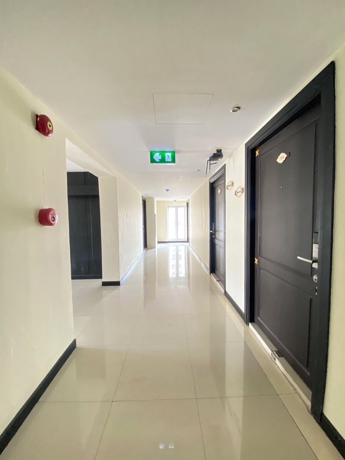 A corridor with a green emergency exit sign, a fire alarm, and a door with a lock.