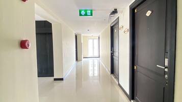 A corridor with a green emergency exit sign, a fire alarm, and a door with a lock.
