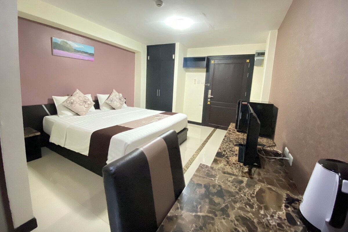 A hotel room with a bed, a desk, a television, and a door.