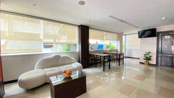 A modern living room with a sofa, a glass coffee table, a dining table with chairs, and a TV mounted on the wall.