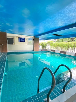 Piscina interna com água azul cristalina, chão ladrilhado e teto azul.