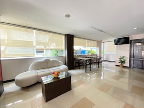 Uma sala de estar moderna com sofá, mesa de centro de vidro, mesa de jantar com cadeiras e televisão fixada na parede.