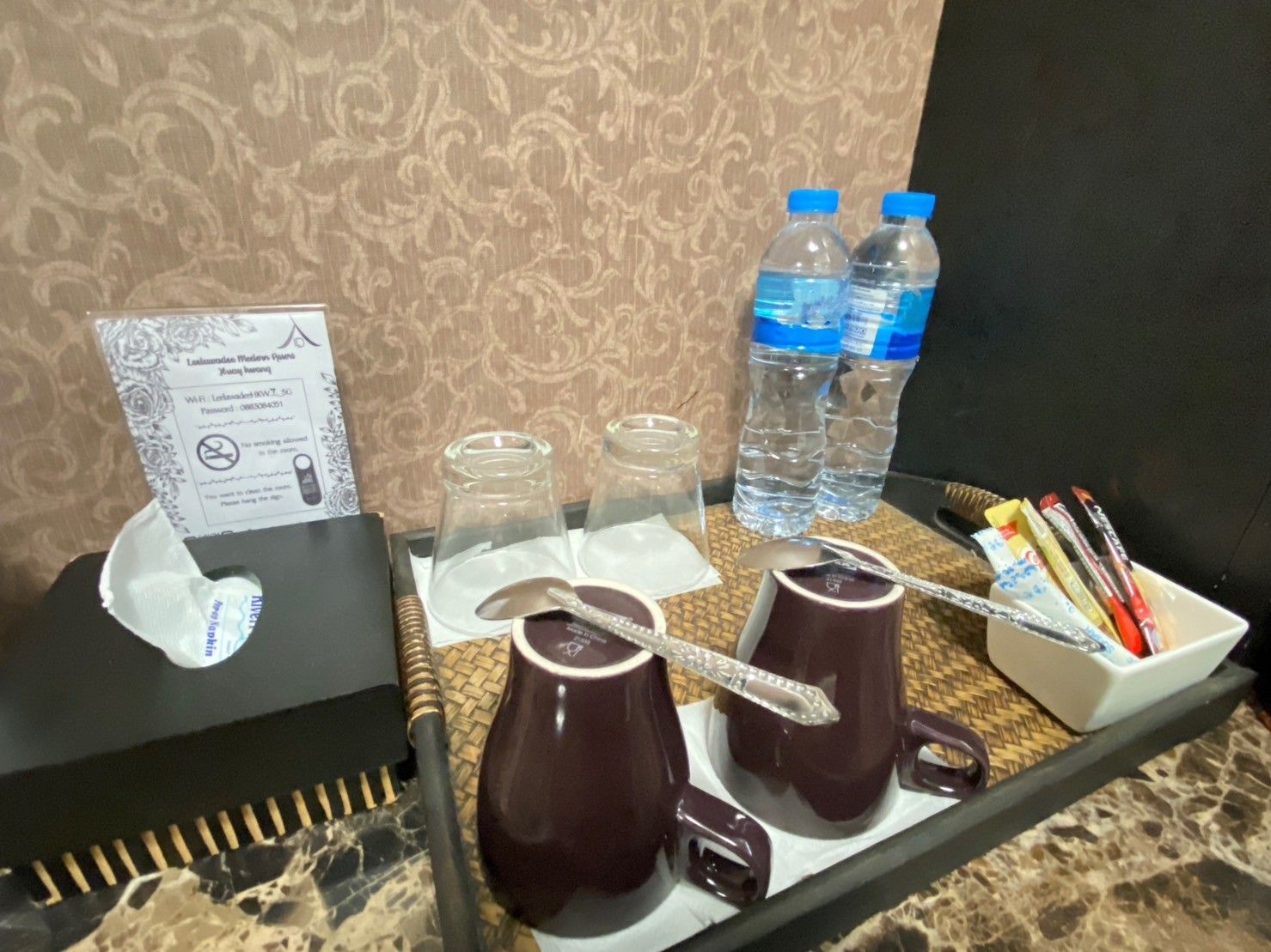 Un plateau contenant une boîte de mouchoirs, deux bouteilles d’eau, deux verres, une cuillère et un récipient rempli d’ustensiles.