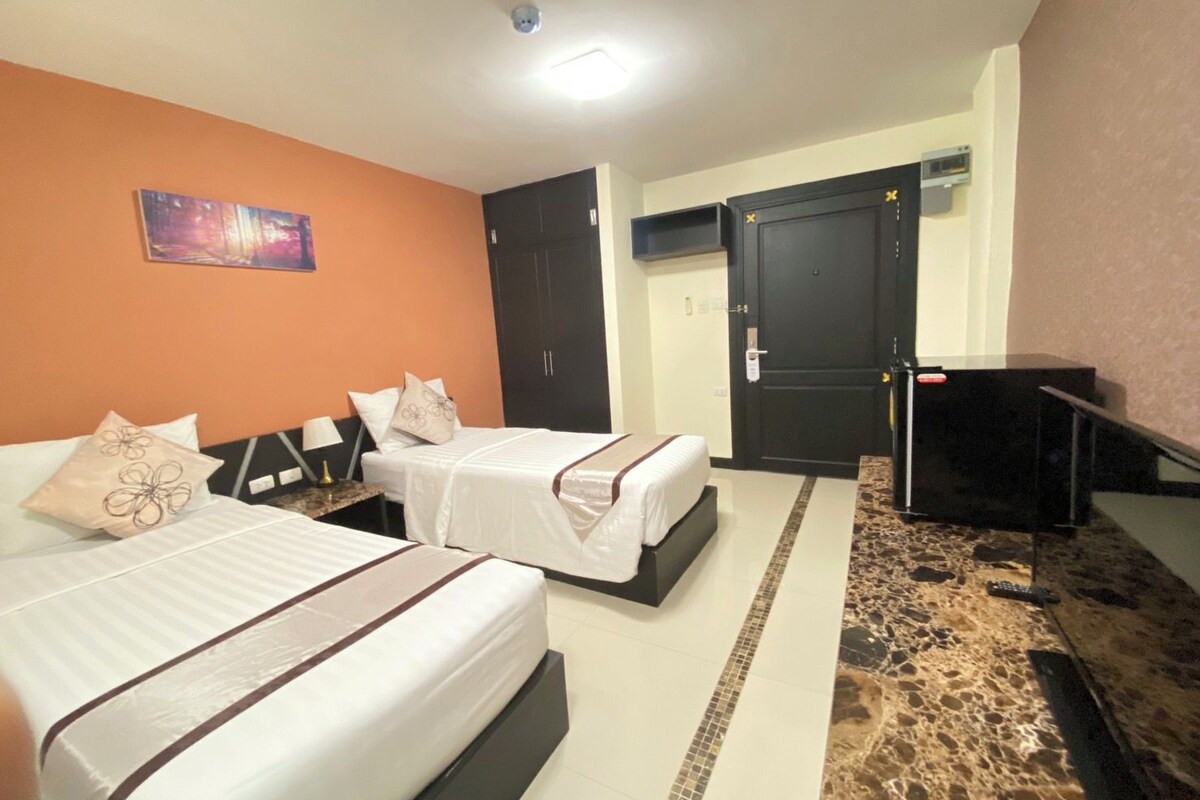 A hotel room with two beds, a television, a wardrobe, and a painting on the wall.