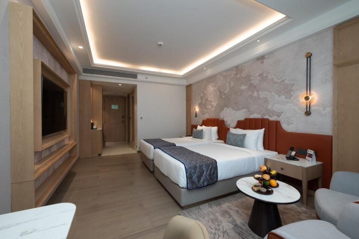 A hotel room with a large bed, a TV, a desk, and a wall-mounted light fixture.