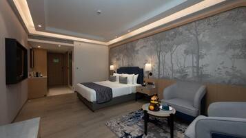 A hotel room with a bed, a seating area with a table, and a wall-mounted TV.