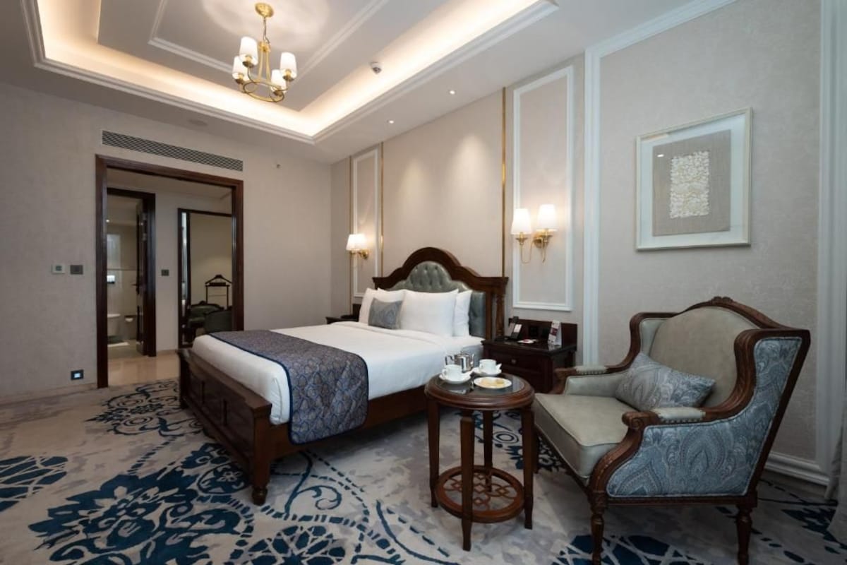 A hotel room with a large bed, bedside table, chair, and a carpeted floor.