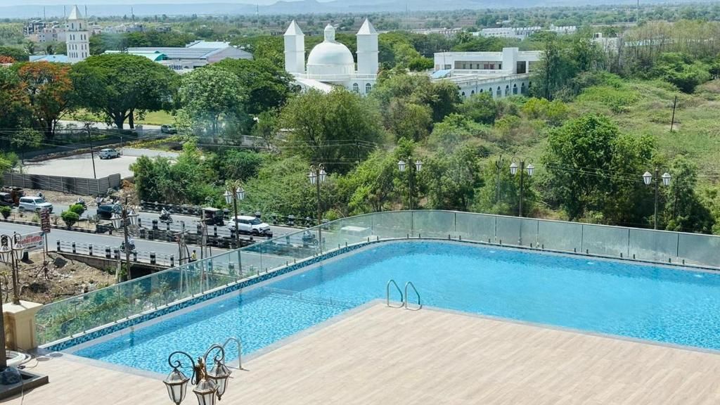 A swimming pool with a glass barrier, surrounded by a wooden deck and outdoor furniture.