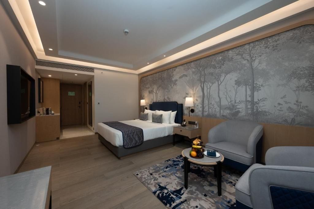 A hotel room with a bed, a seating area with a table, and a wall-mounted TV.