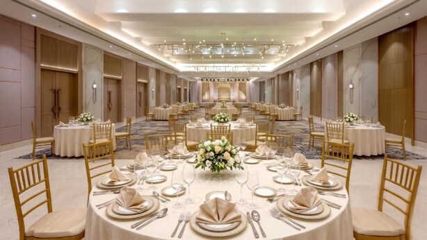 A banquet hall with round tables, gold chairs, and a central floral arrangement.