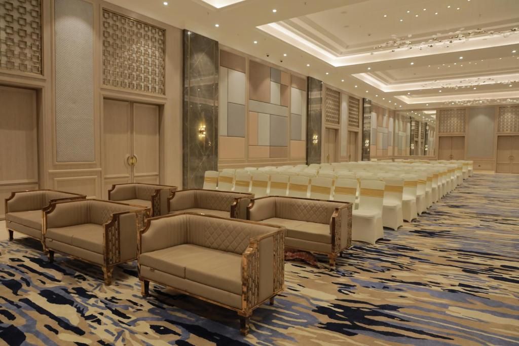 A hotel lobby with a patterned carpet, seating area with sofas and chairs, and a large white block of seating.