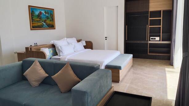 A hotel room with a bed, a sofa, a desk, a painting, and a wardrobe.