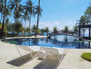 A pool area with lounge chairs, a bridge, and palm trees.