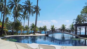 A pool area with lounge chairs, a bridge, and palm trees.