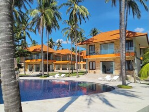 A resort with a swimming pool, palm trees, and a building with a tiled roof.