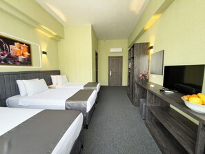 Habitación de hotel con dos camas, un escritorio con un cuenco de fruta, un televisor y un cuadro en la pared.