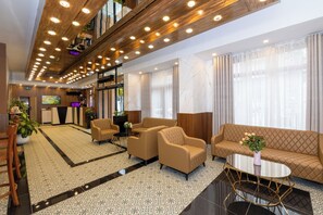 Hall d'hotel dal design moderno, con reception, area salotto con divani e poltrone, tavolino da caffè e pavimento a motivi decorativi.