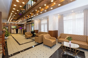 Un hall d’hôtel au design moderne, comprenant un comptoir d’accueil, un espace salon avec des canapés et des fauteuils, une table basse et un sol à motifs.