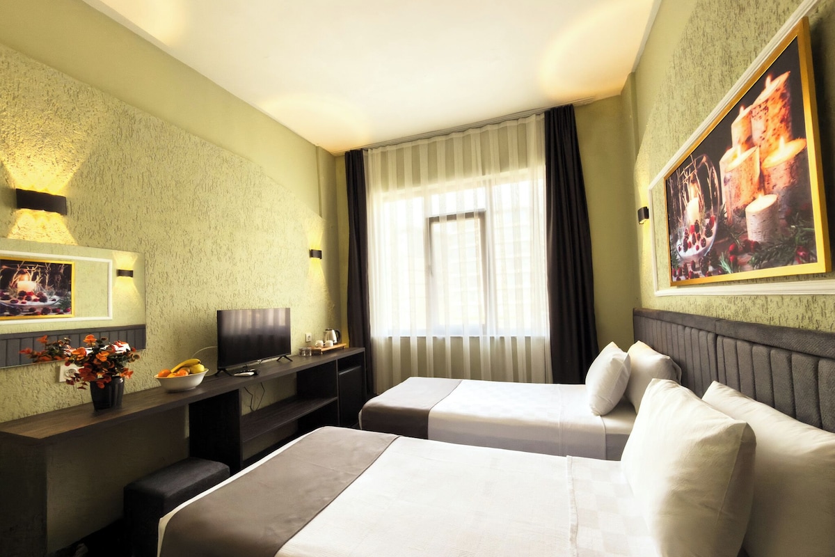 A hotel room with two beds, a television, a desk with a computer, and a window with curtains.