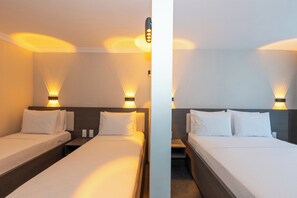 Camera d'albergo con due letti, entrambi con lenzuola e cuscini bianchi, e lampade a parete che creano una luce soffusa.