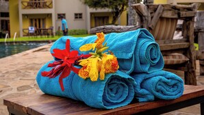 Un munt de tovalloles blaves amb un floreiximent vermell i groc sobre una banca de fusta a prop d'una zona de piscina.