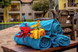 A stack of blue towels with a red and yellow flower on a wooden bench near a poolside area. - Weruweru River Lodge (Moshi)