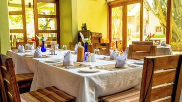 Uma sala de jantar com uma mesa comprida posta para refeição, rodeada por cadeiras de madeira.