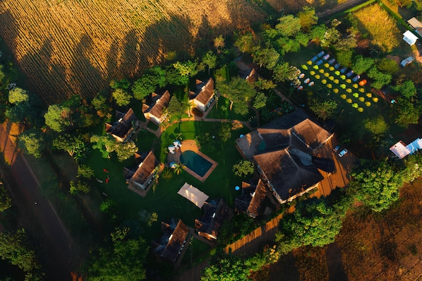 An aerial view of a property with multiple buildings, a swimming pool, and a garden area with boats.