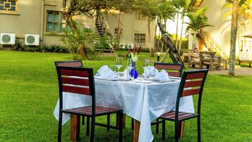 An outdoor dining area with a table set for four, surrounded by chairs, in a lush garden setting with a building in the background.