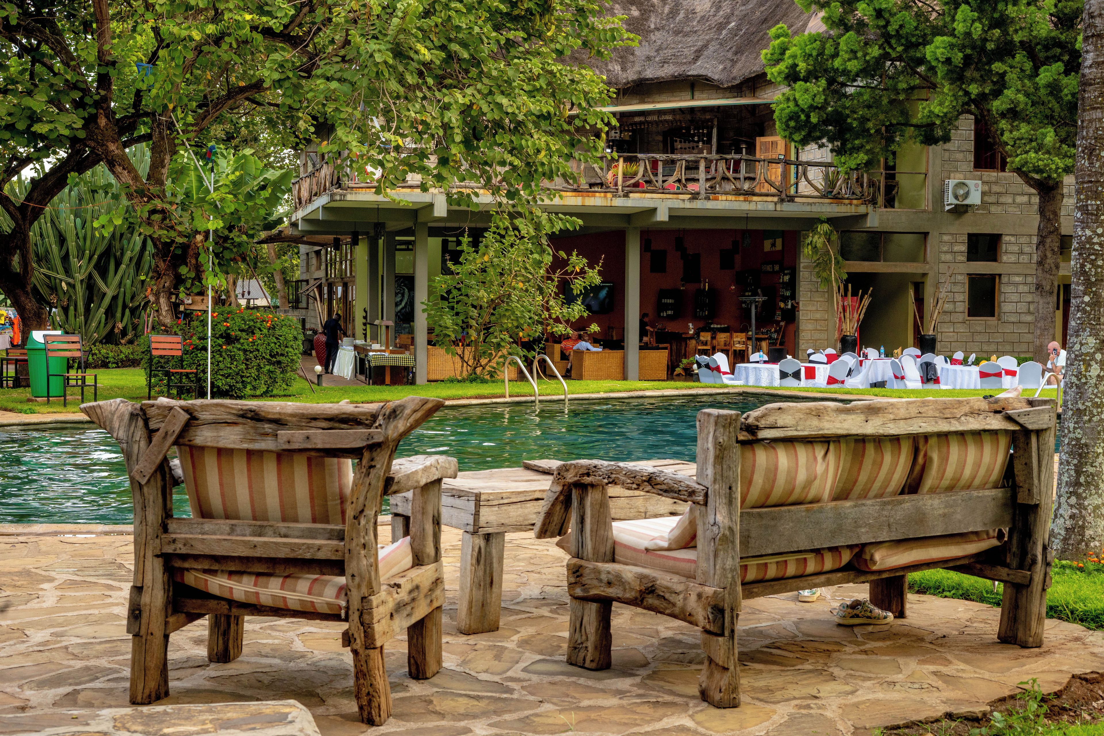 A poolside area with wooden furniture and a building with a thatched roof in the background.