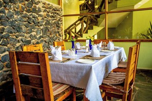 A table set for dining with a stone wall backdrop, wooden chairs, and a view of a staircase.