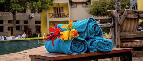 A poolside area with a wooden table holding rolled towels and a bouquet of flowers.