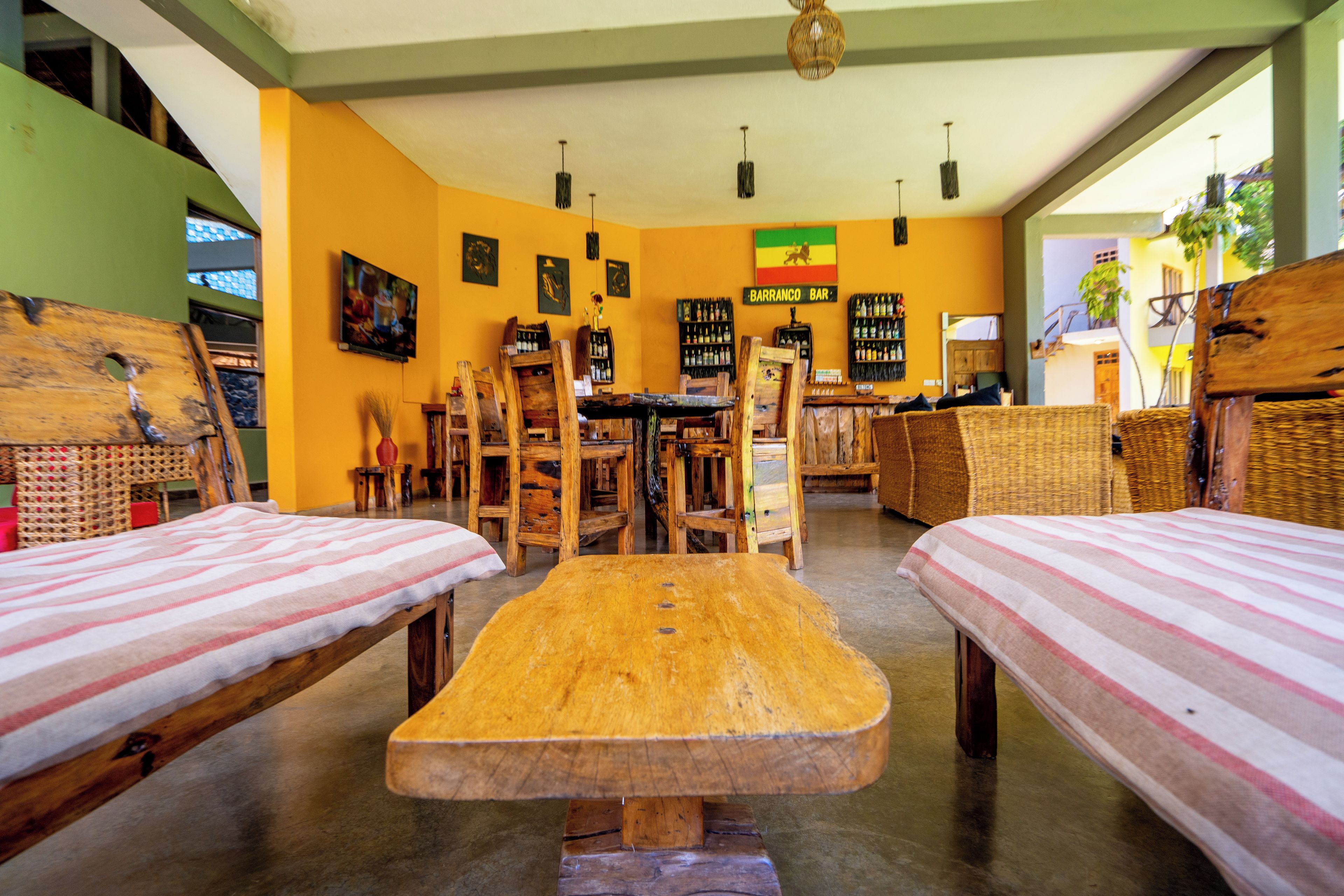 A room with two wooden beds, a central table, and a bar area with shelves of bottles.