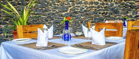 A table set for four with white tablecloths, blue vases, and a stone wall background.